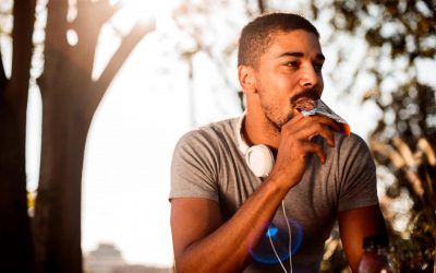 Young man eating candy bar African-American male with headphones eating chocolate candy bar while resting from outdoor exercise.