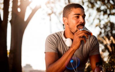 African-American male with headphones eating chocolate candy bar while resting from outdoor exercise.