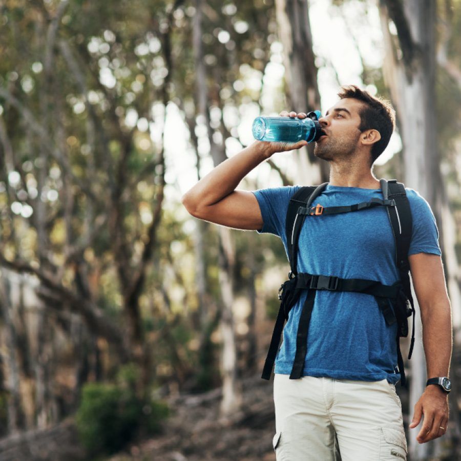 sportis-boisson-proteinee Cropped shot of a carefree young man drinking water from a bottle while going for a hike up a mountain
